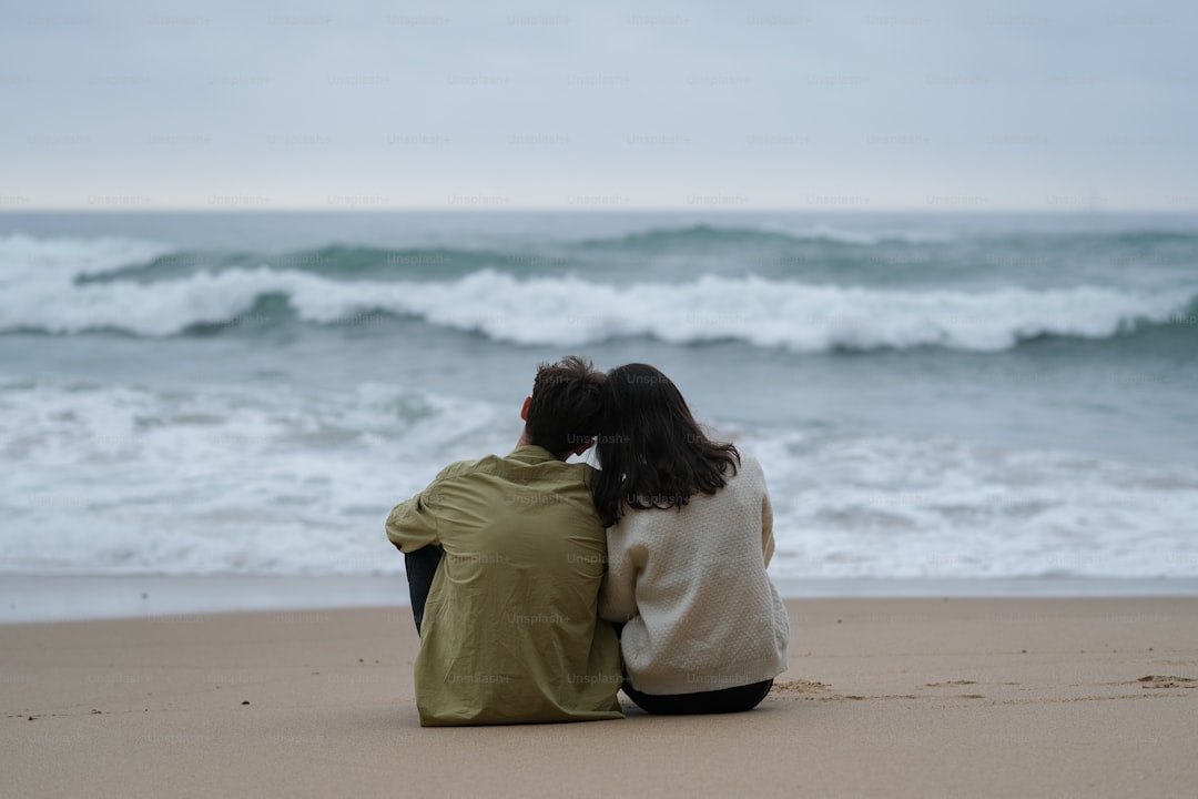 a couple of people sitting on top of a sandy beach