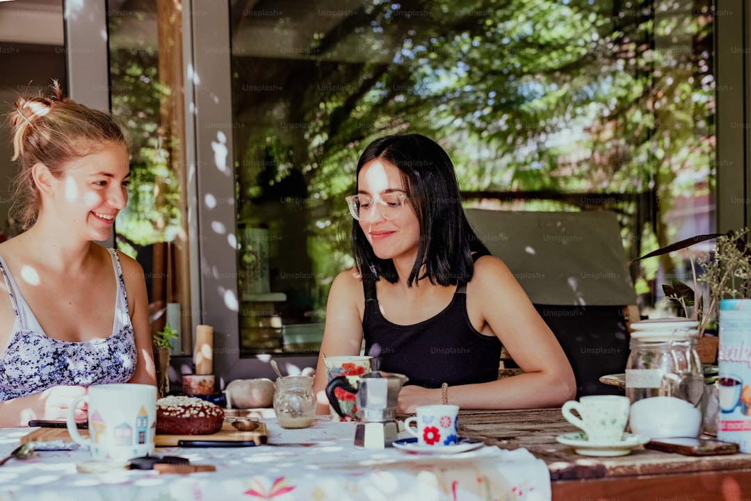 a couple of women sitting at a table with cups