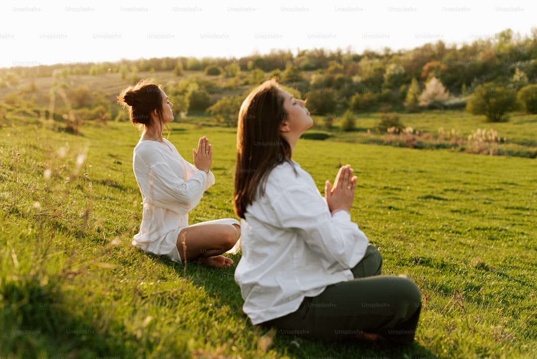 a couple of women sitting on top of a lush green field