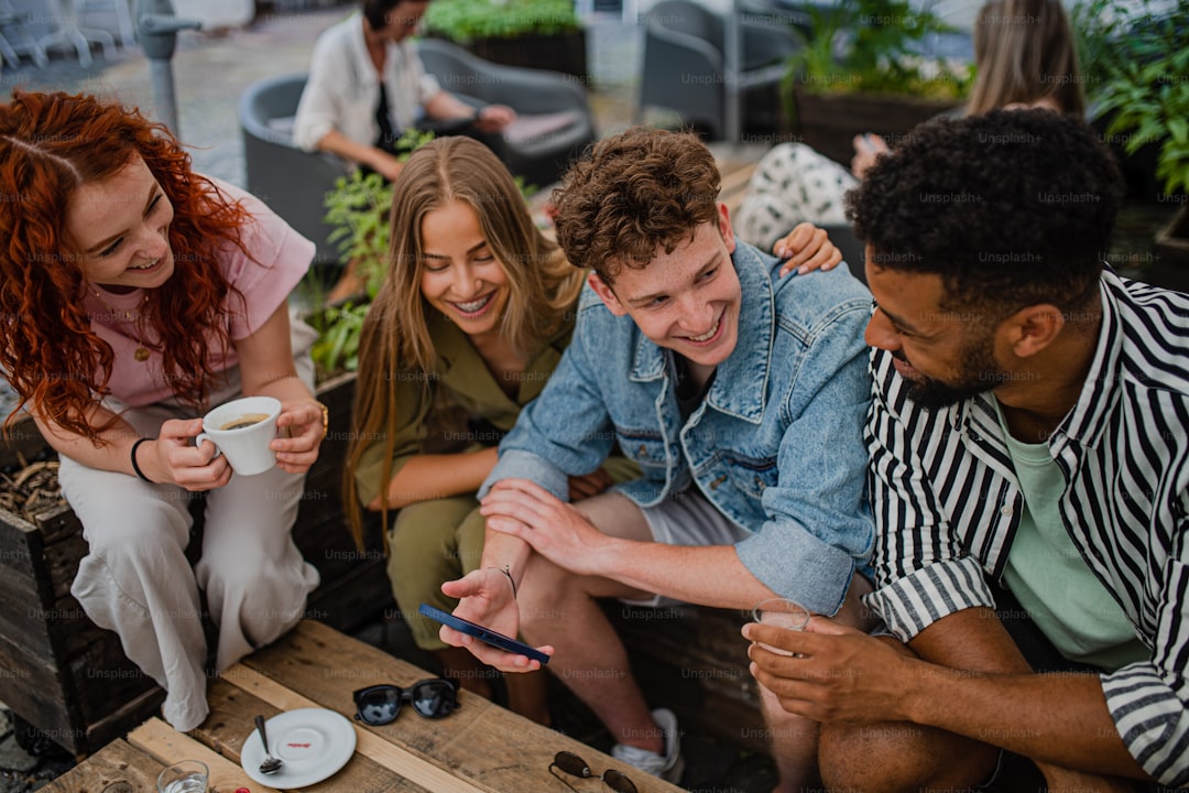 A group of happy young people sitting in outdoors cafe on town trip, talking.