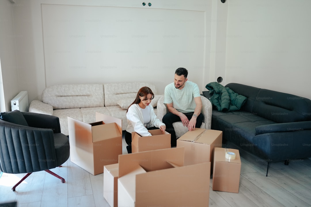 a man and woman sitting on a couch surrounded by boxes