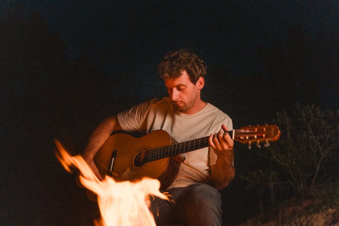 a man playing a guitar in front of a fire