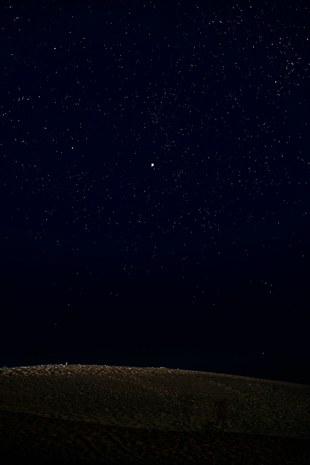 A man standing on top of a hill under a night sky filled with stars