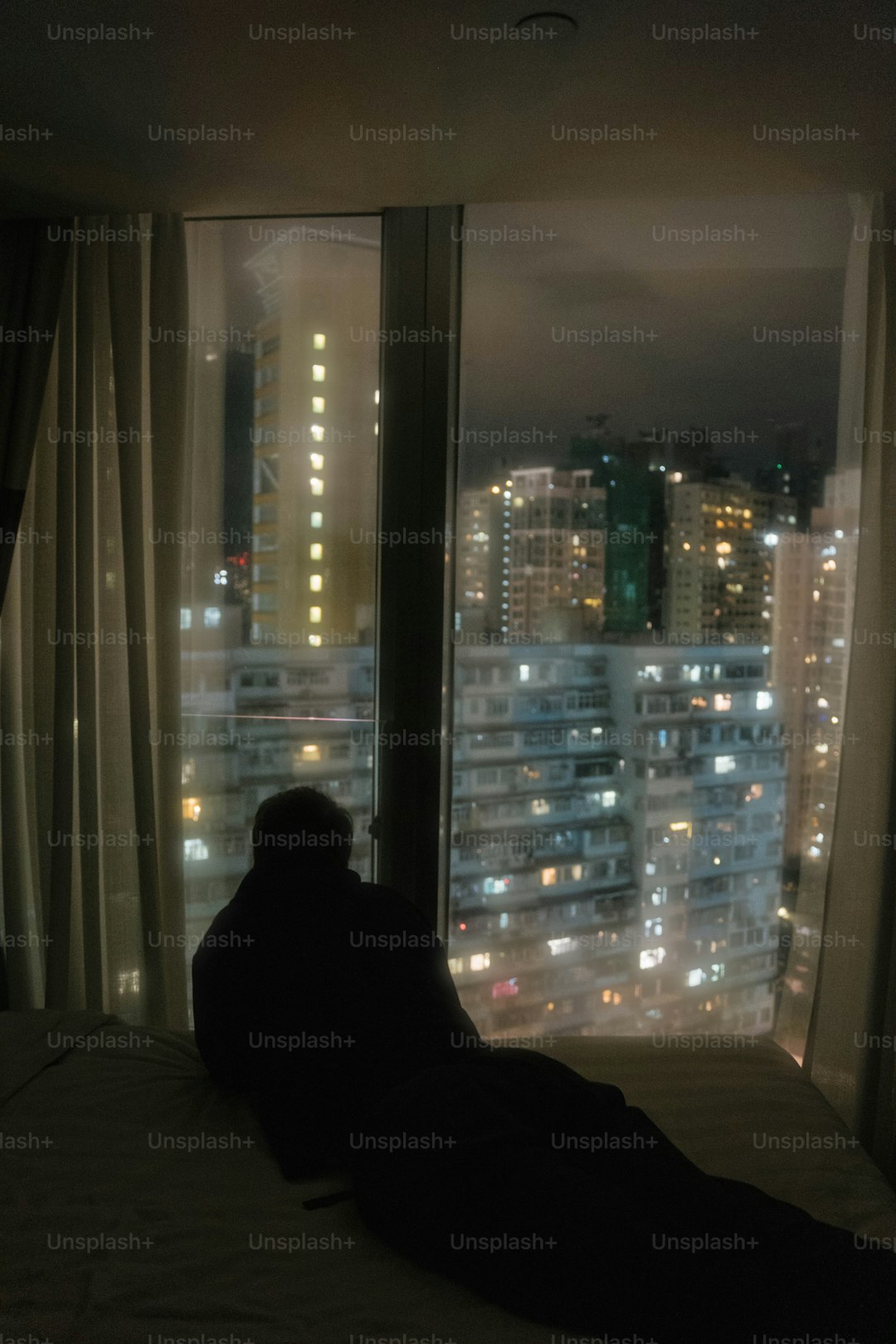 A person sitting on a bed looking out a window