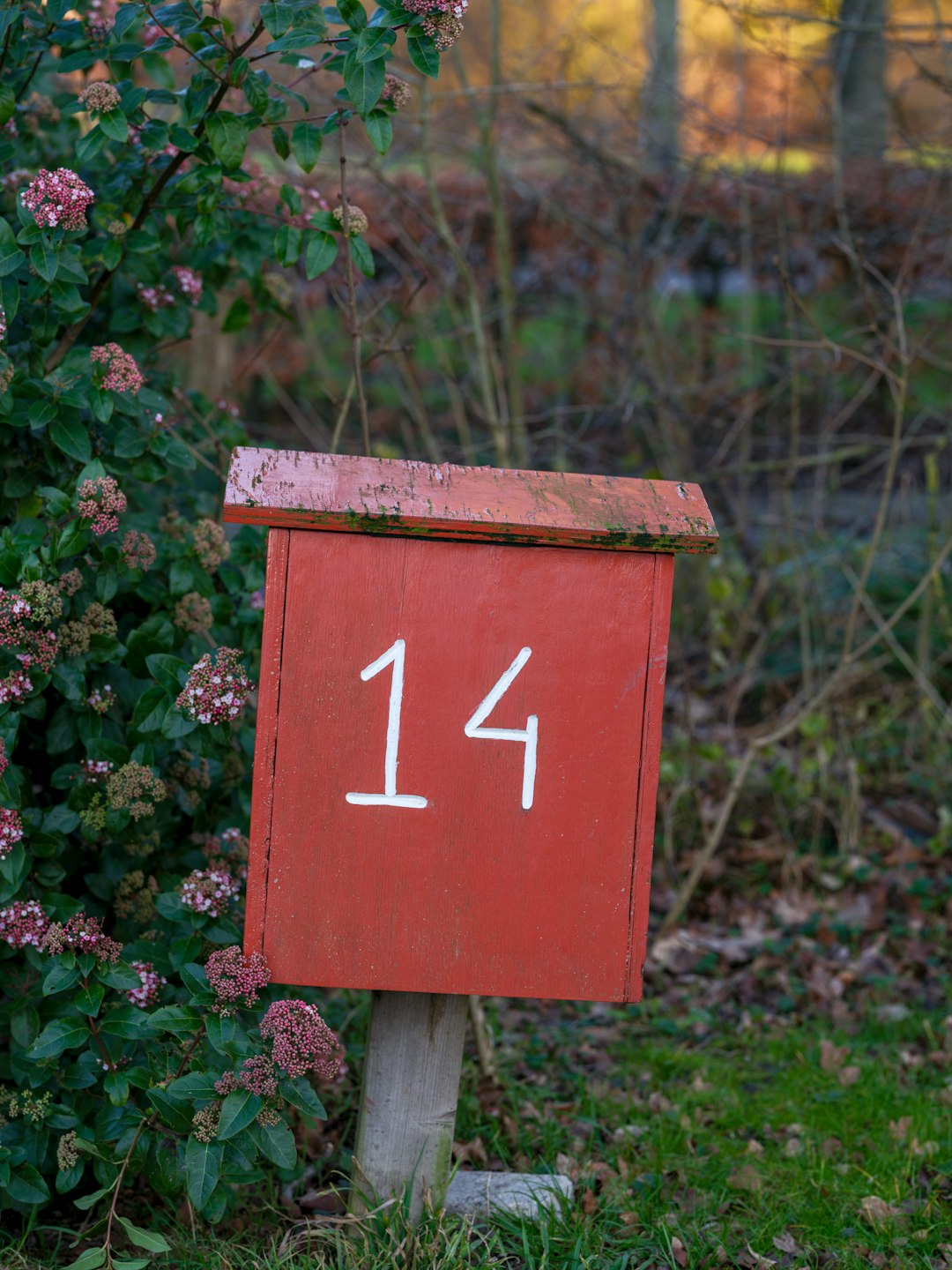 A red mailbox sitting next to a bush