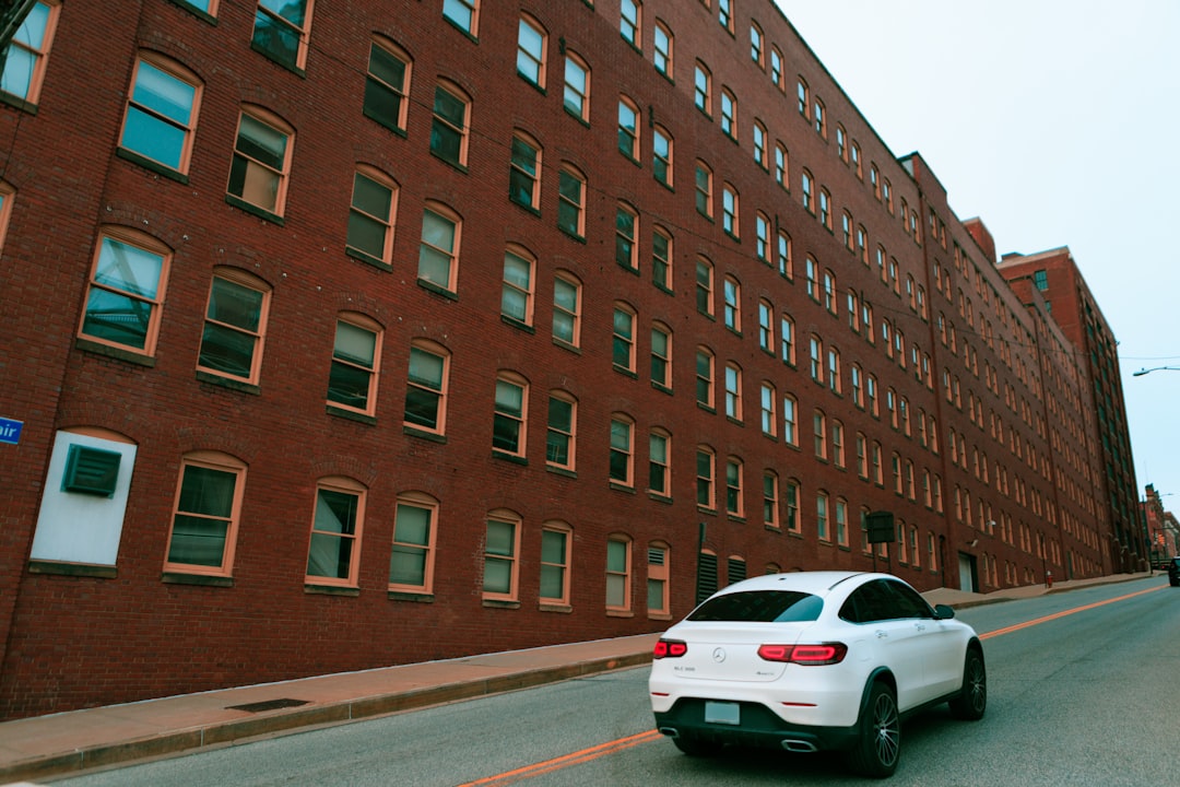 a white car driving down a street next to a tall brick building