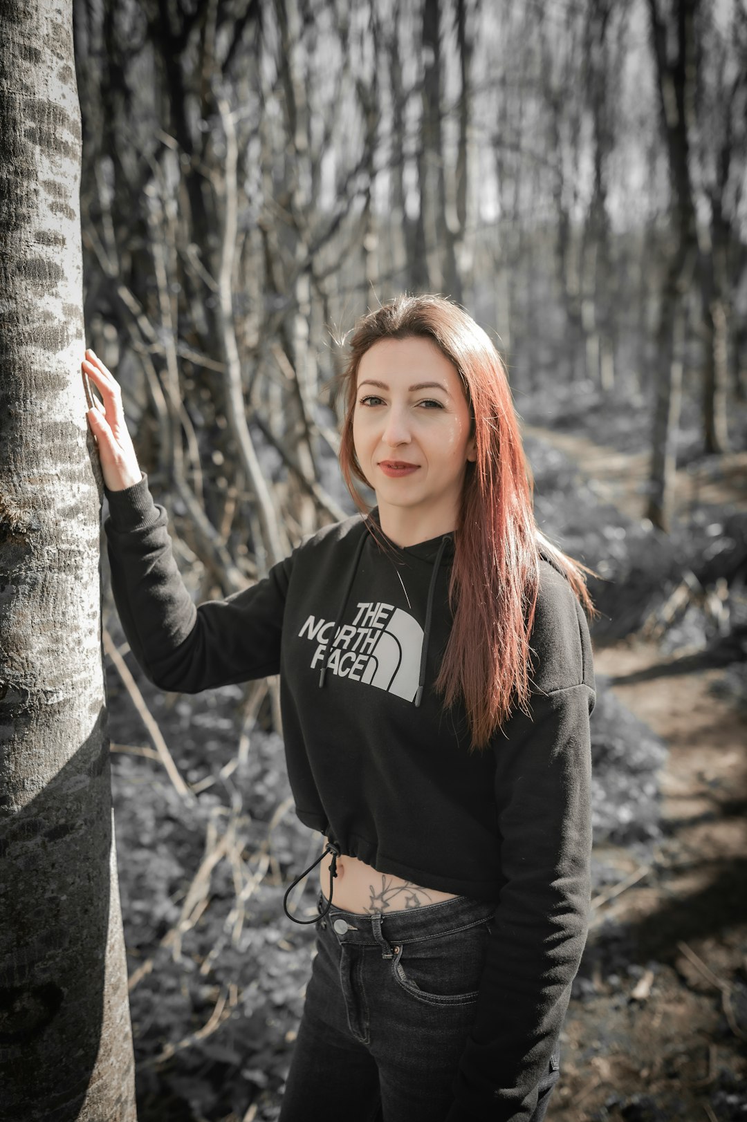 a woman standing next to a tree in a forest