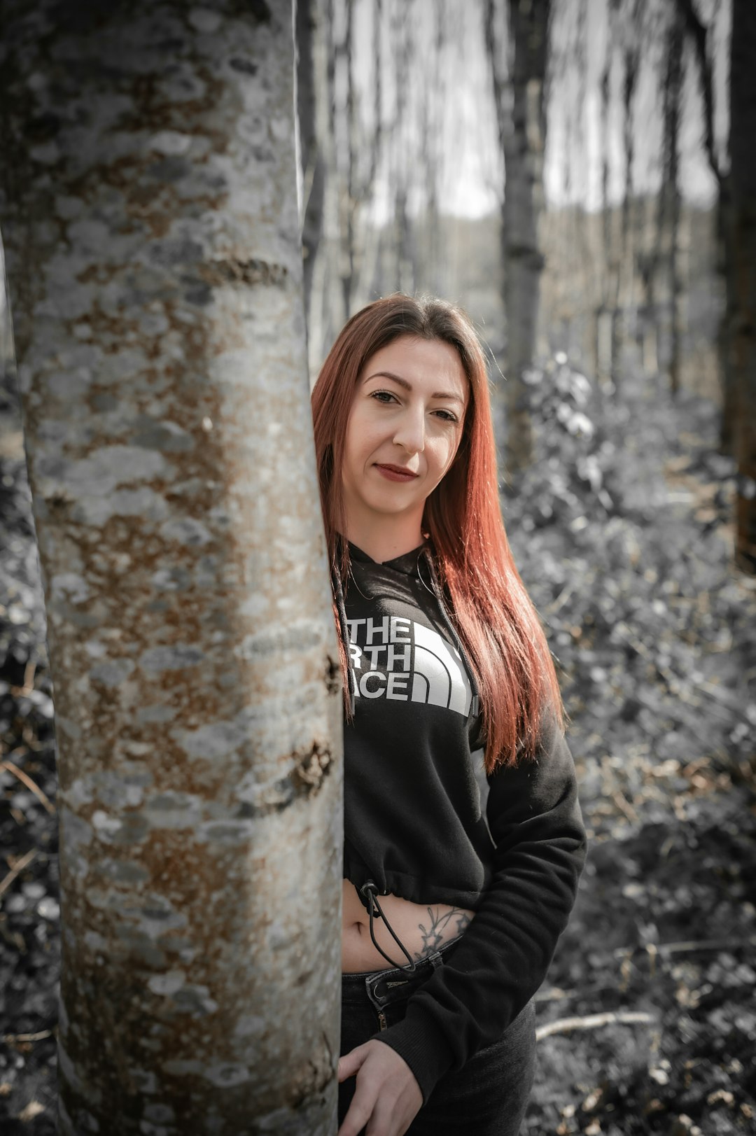 a woman standing next to a tree in a forest