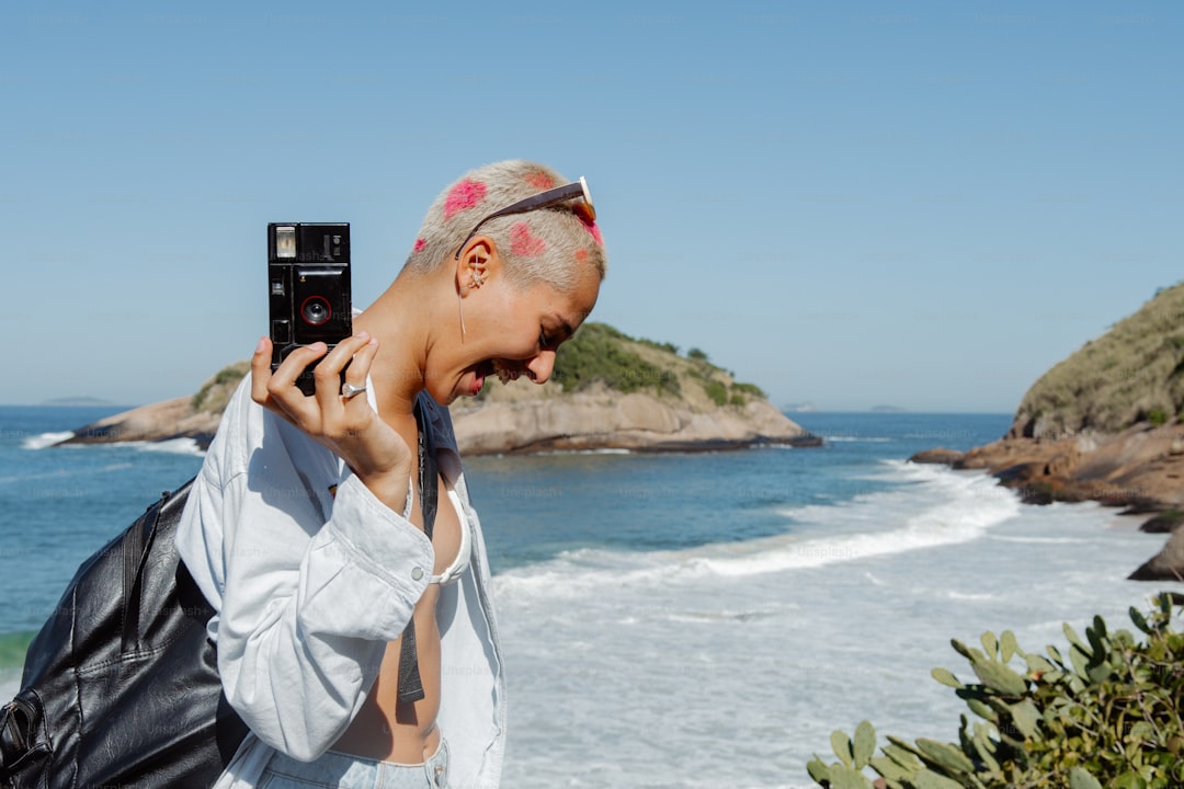 a woman taking a picture of the ocean with her cell phone