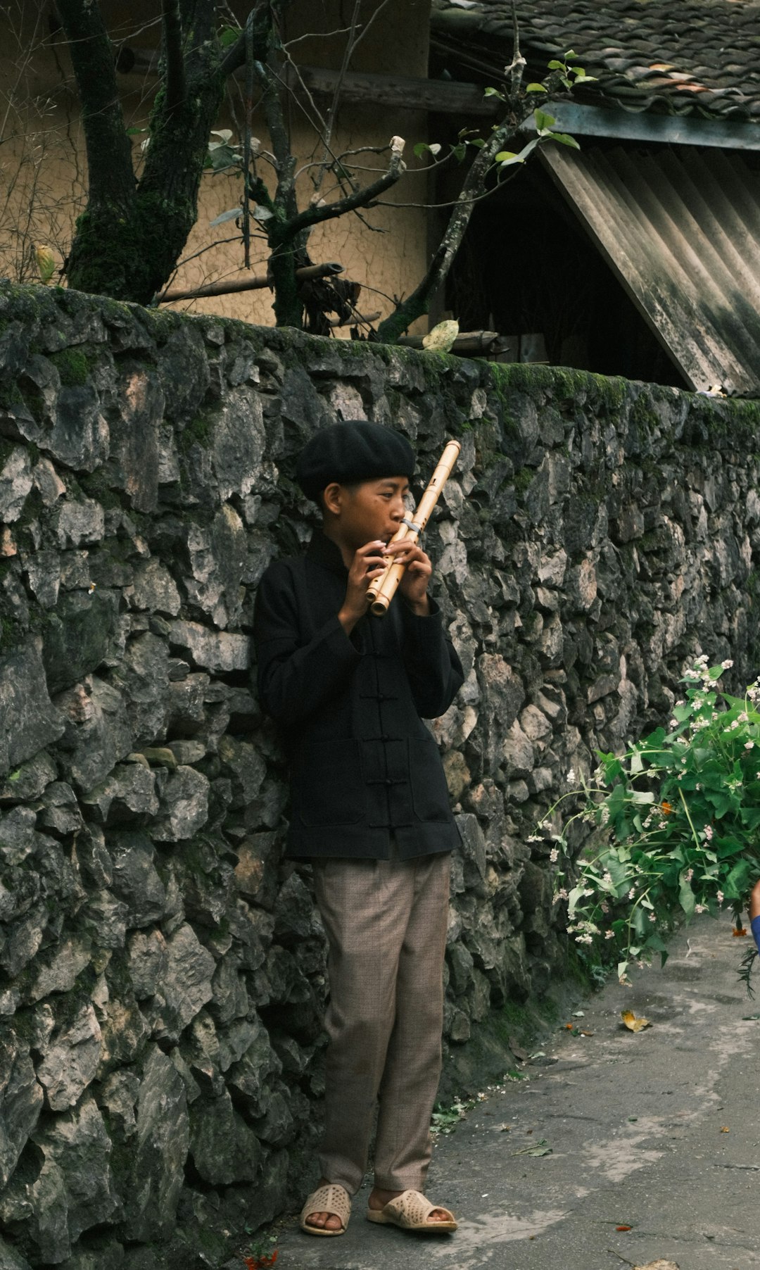 a young boy standing next to a stone wall holding a baseball bat