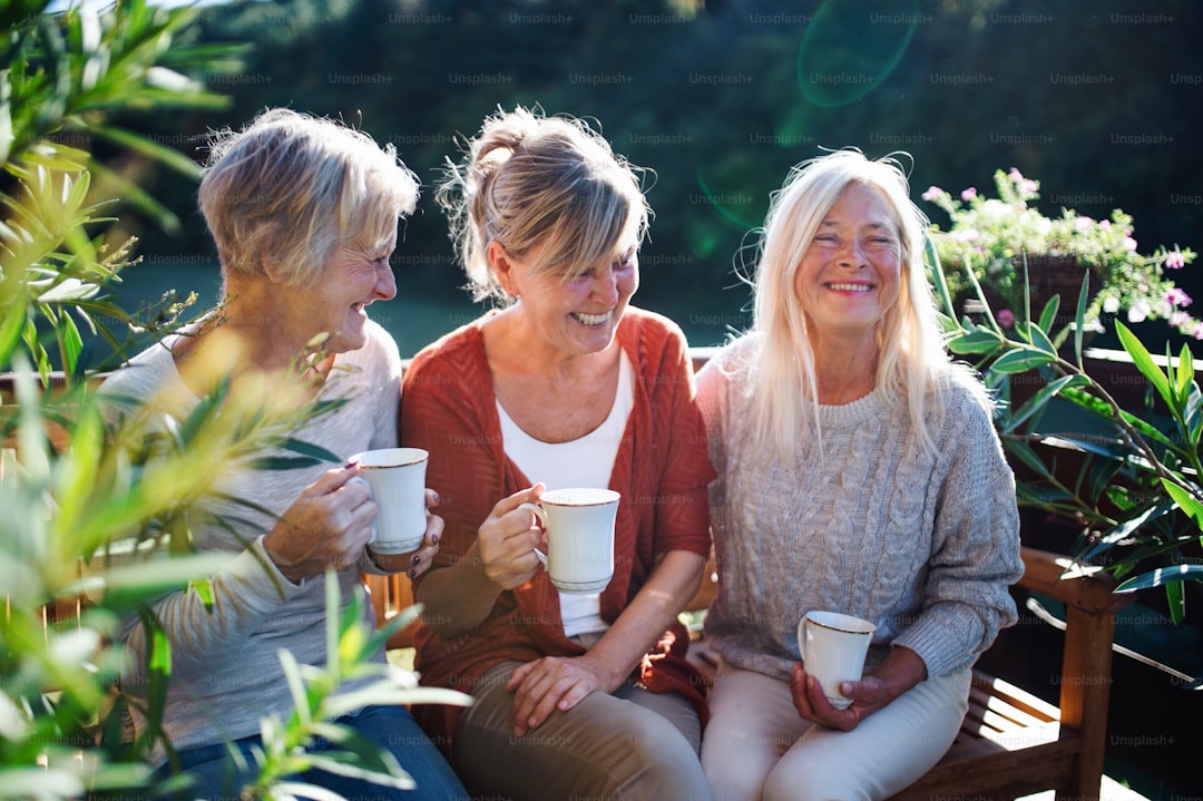 Group of senior women friends with coffee sitting outdoors on terrace, resting.