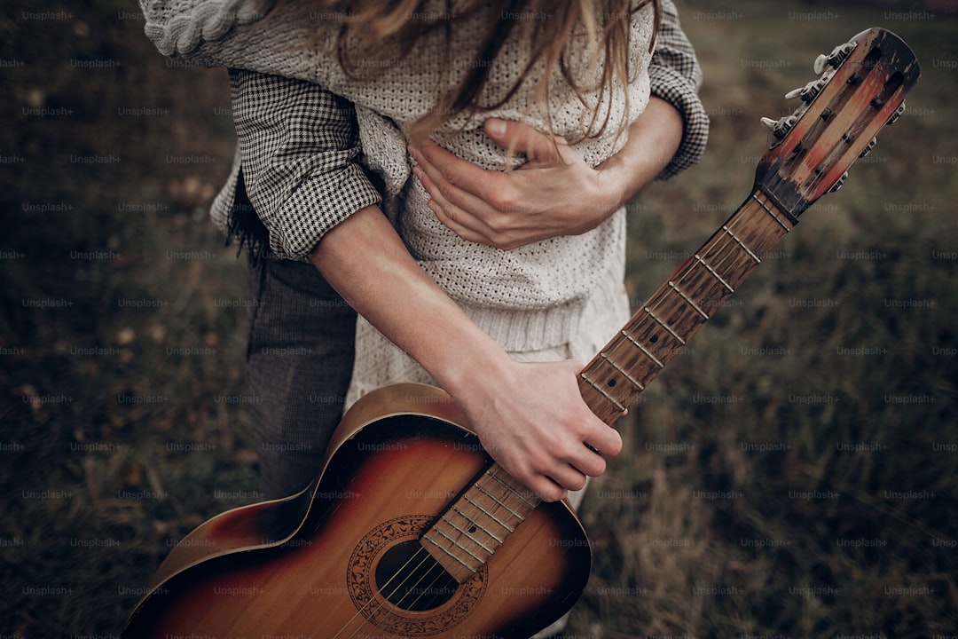 Hipster musician couple hugging in field, handsome man embracing gypsy woman in white dress, guitar closeup