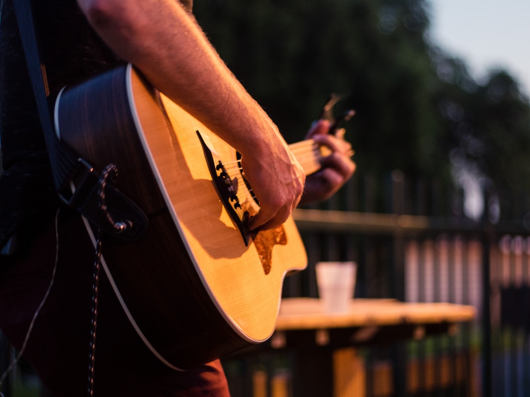 man in black t-shirt playing brown acoustic guitar