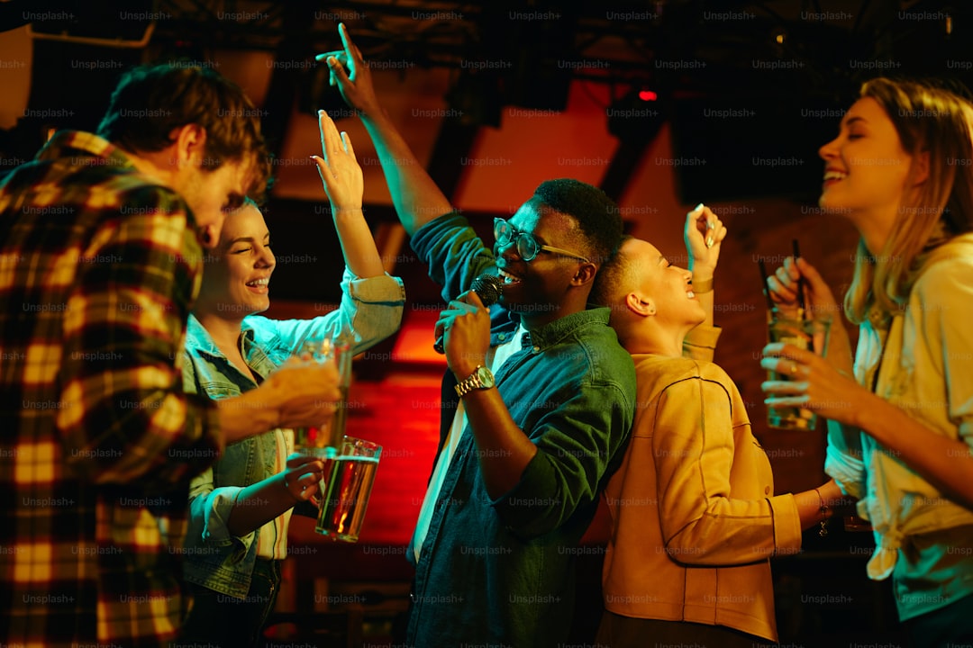 Multi-ethnic group of young people having fun and singing karaoke in a bar at night. Focus is on black man.