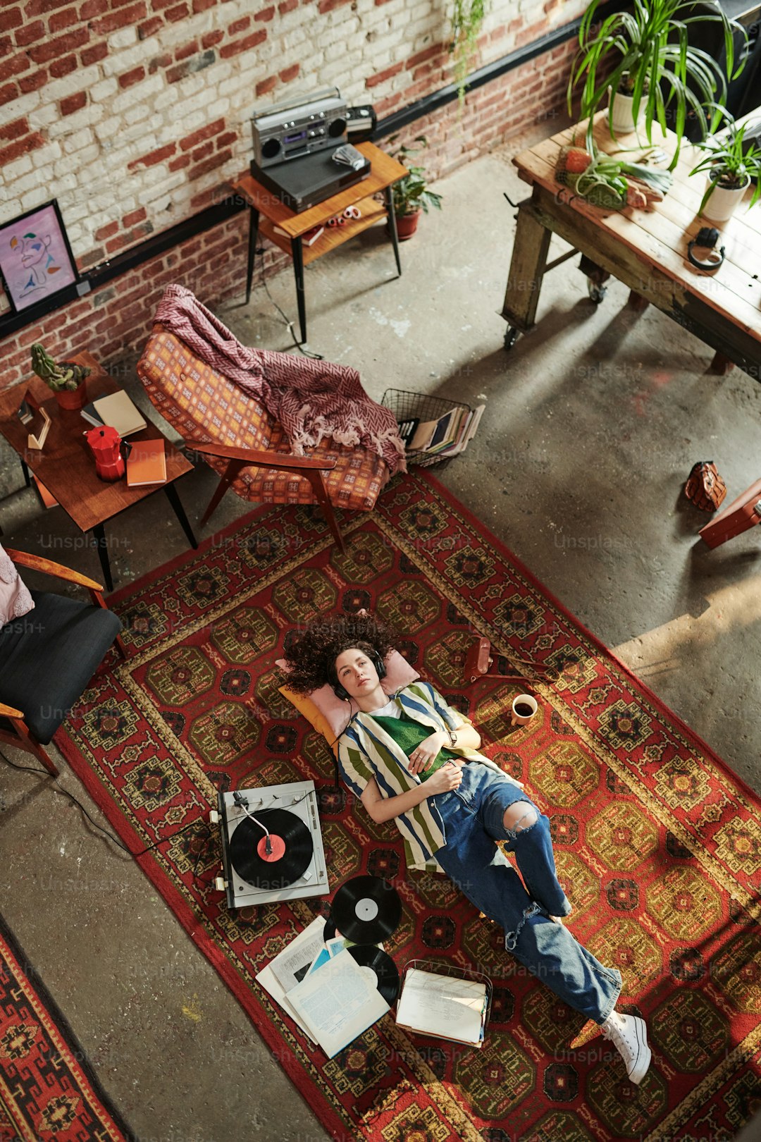 Overview of young woman in stylish casualwear resting on the floor while enjoying music on vynil disks being played on record player