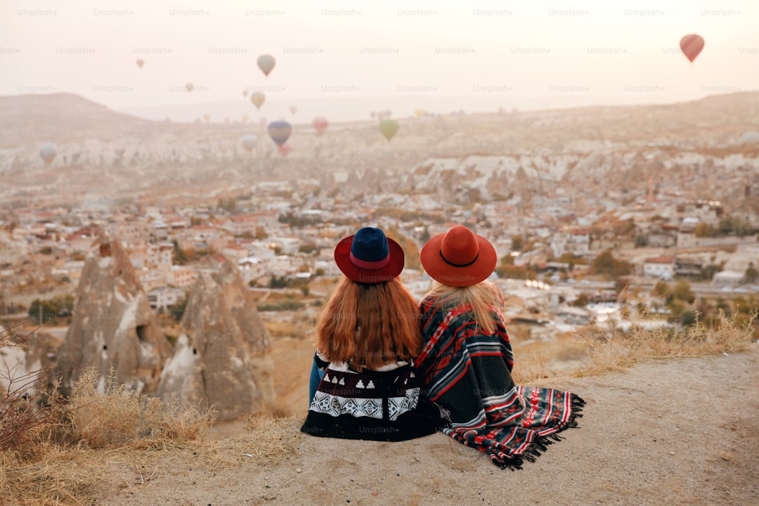 People Travel. Women In Hats Sitting On Hill Enjoying Flying Hot Air Balloons View At Cappadocia Turkey. High Resolution