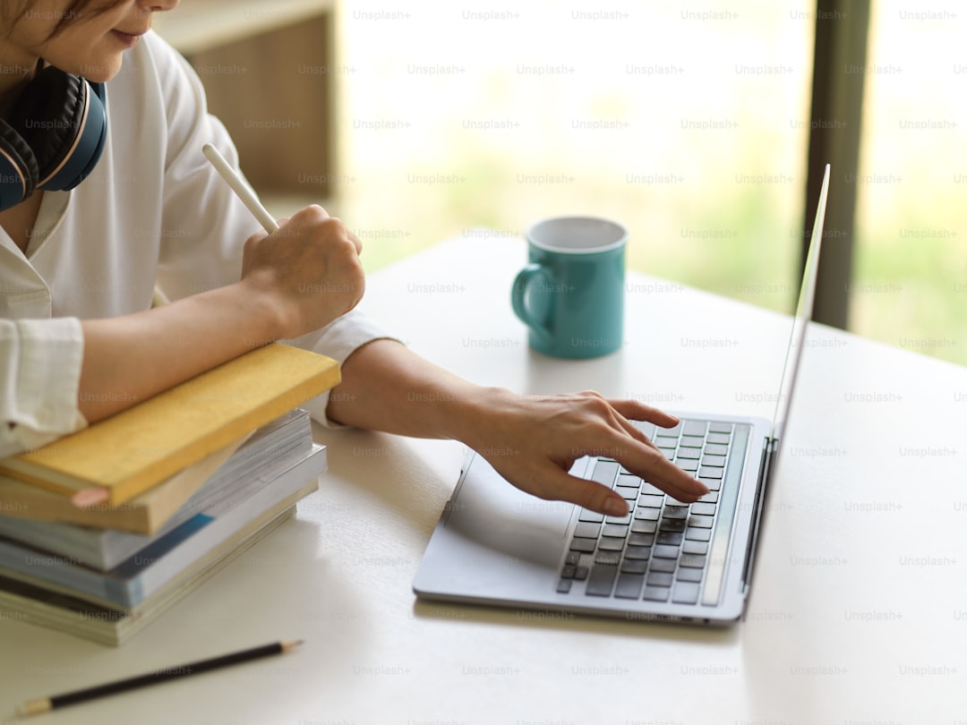 Side view of female university student online studying with laptop and stack of books in living room at home