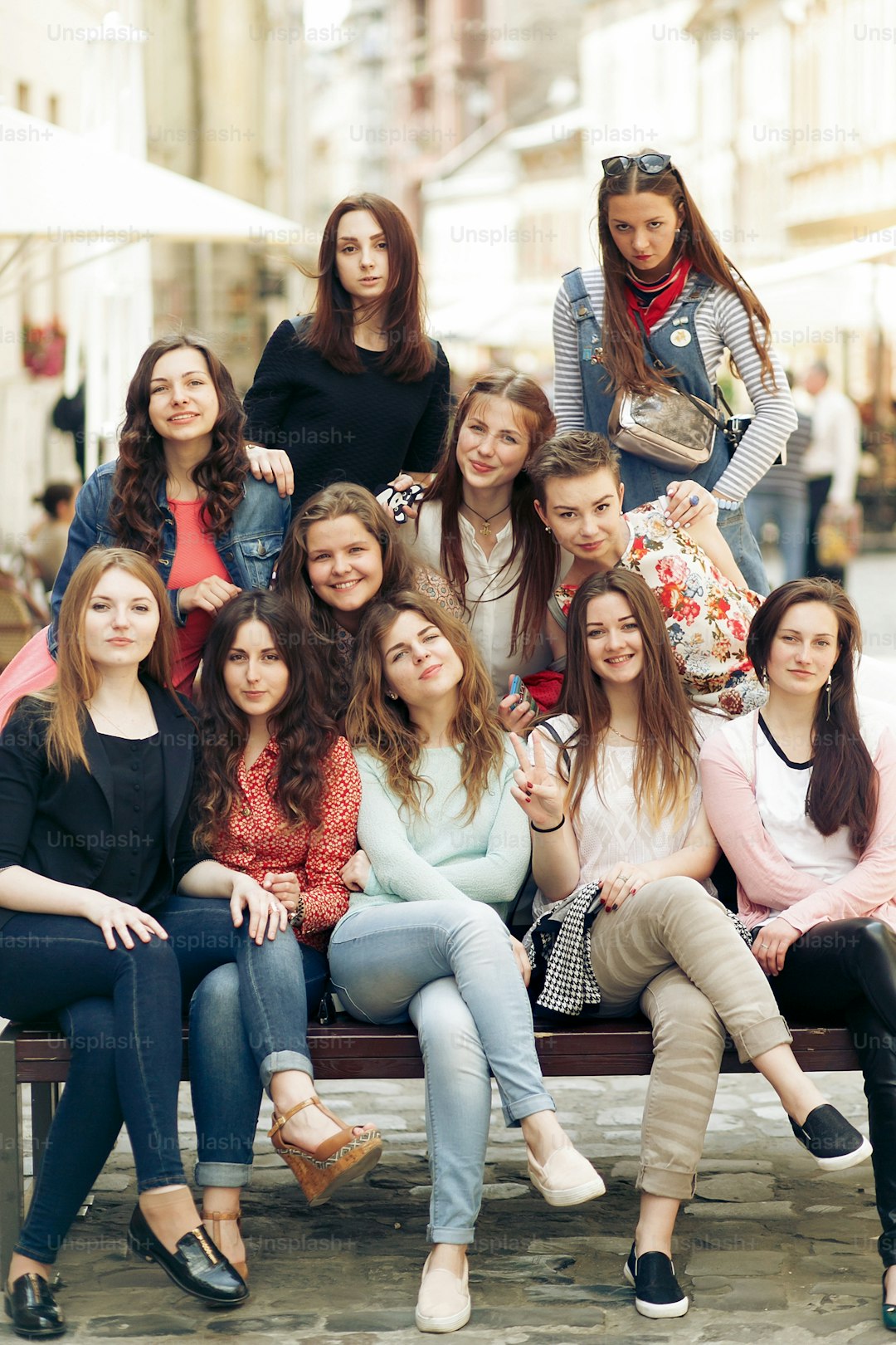 stylish happy women hipsters fashionable dressed smiling and sitting on bench in europe city street, joyful moments friendship concept