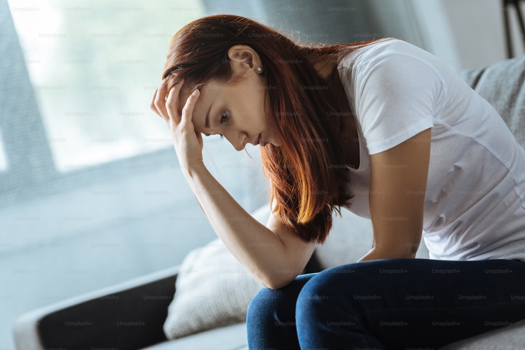 Tough problem. Cheerless upset unhappy woman sitting on the sofa and holding her forehead while looking for a solution of her problem