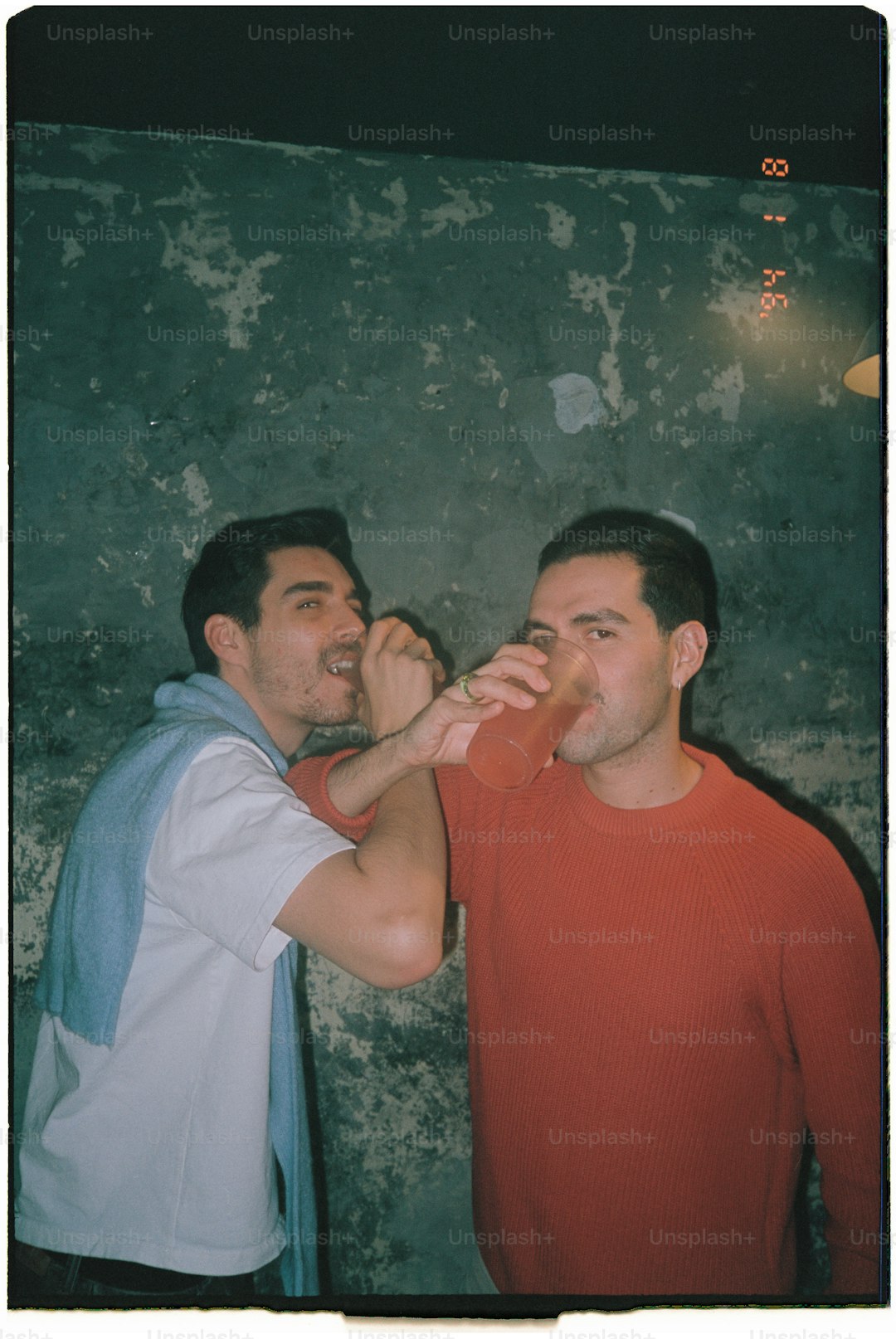 Two men drinking a beverage together.