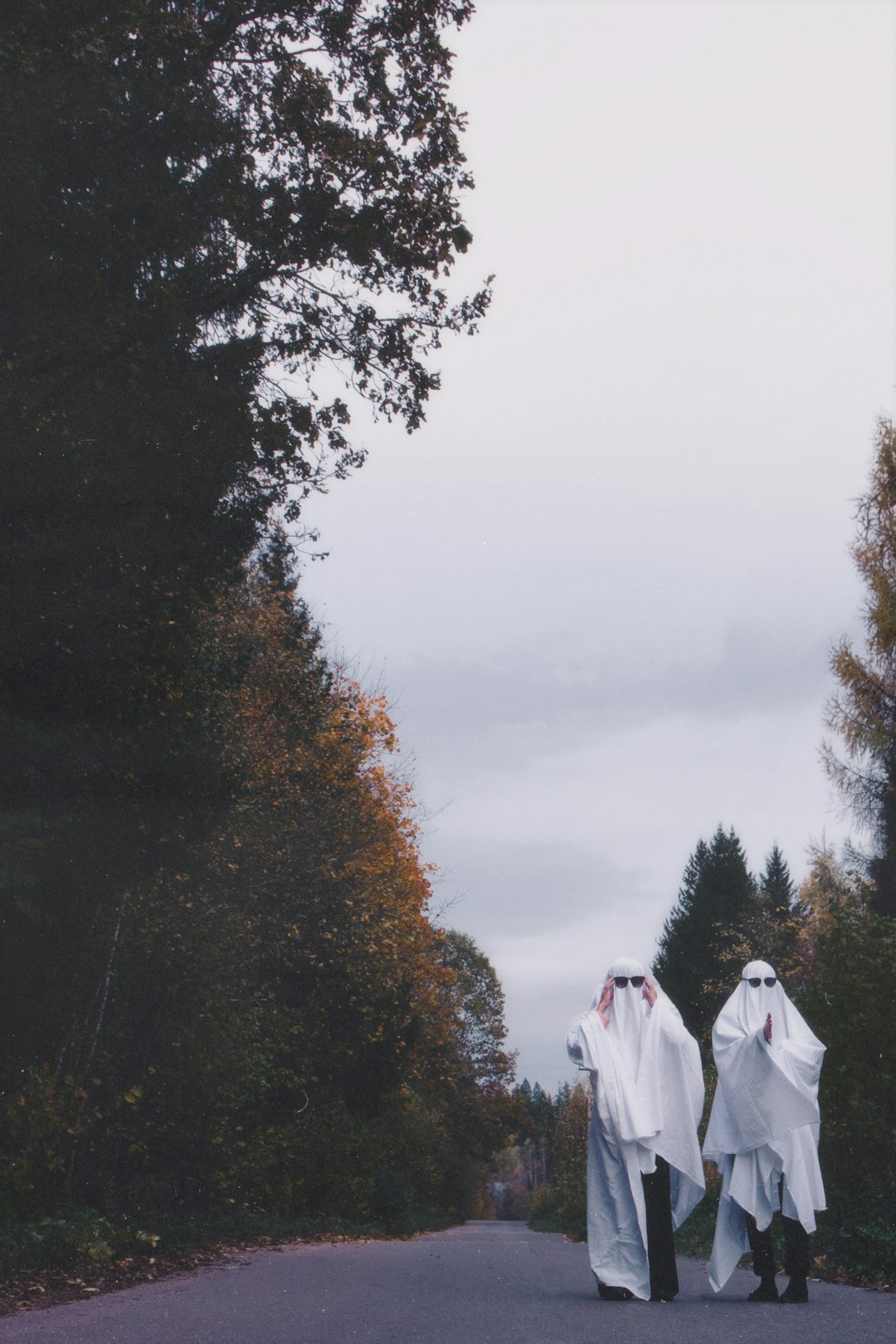 Two people dressed in ghost costumes walking down a road