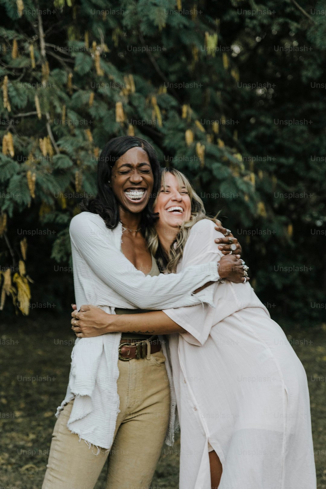 two women hugging each other in front of trees