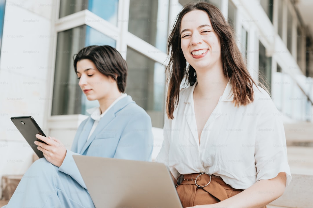 two women sitting on steps with a laptop