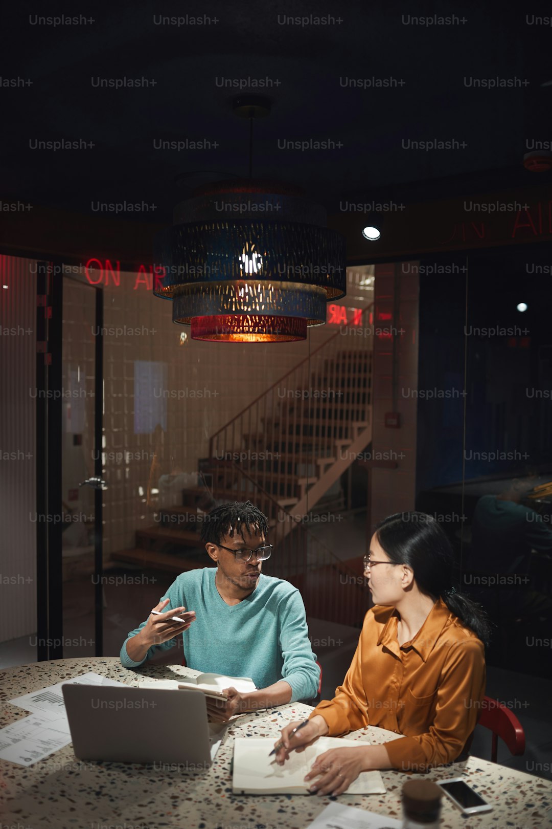 Wide angle portrait of two ethnic business people discussing project while working late in dark office, copy space