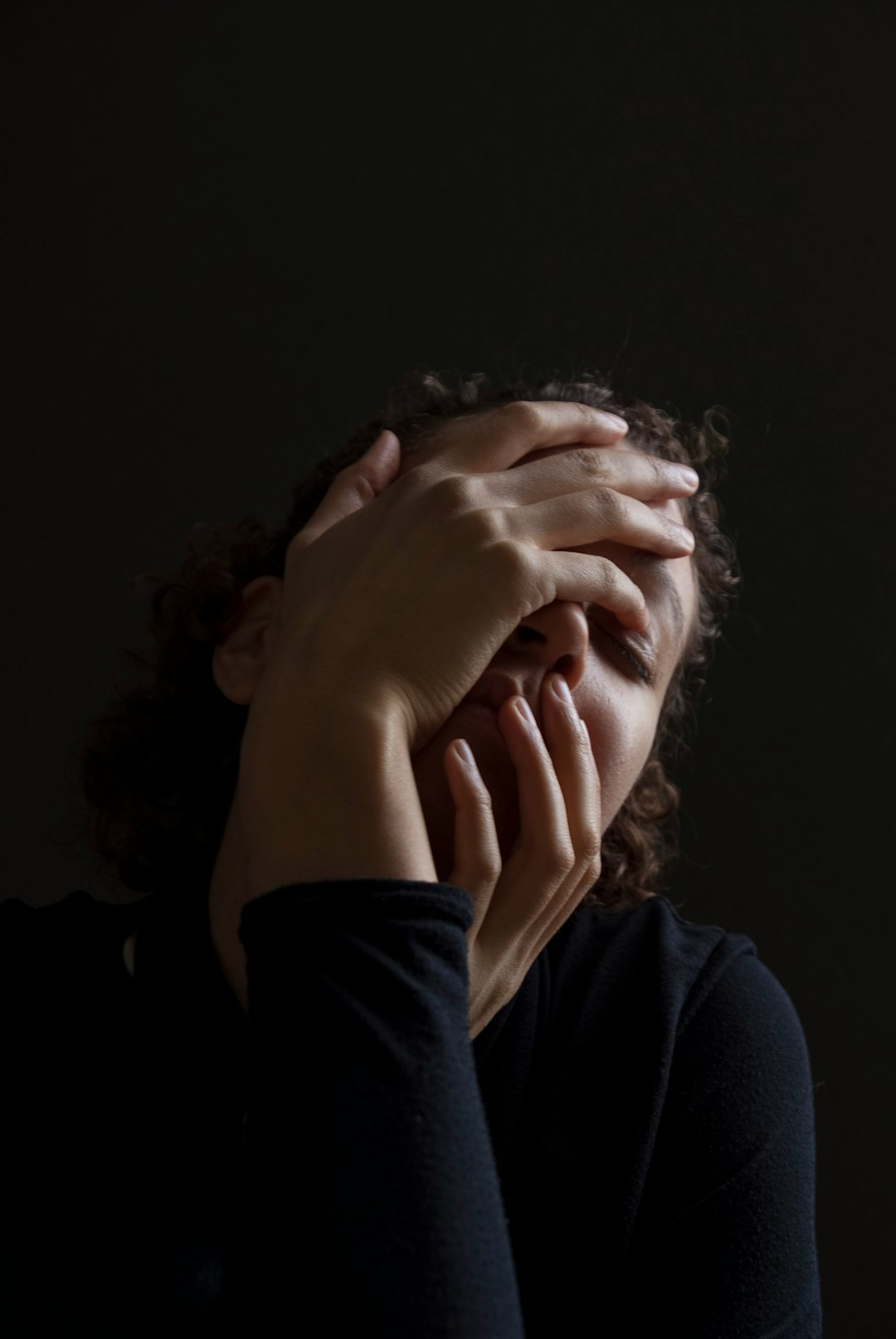 woman wearing blue long-sleeved shirt touching her face