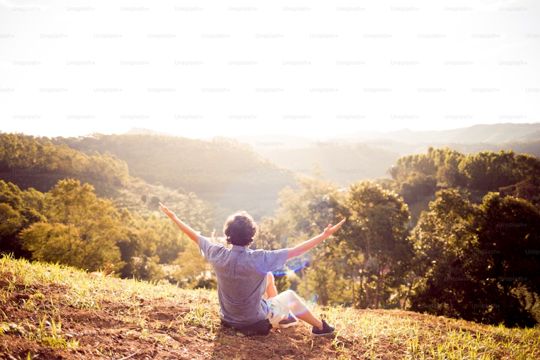 Young man on the top of a mountain with arms raised and with the sunset in the background. Concept of happiness, gratitude, success and well being.