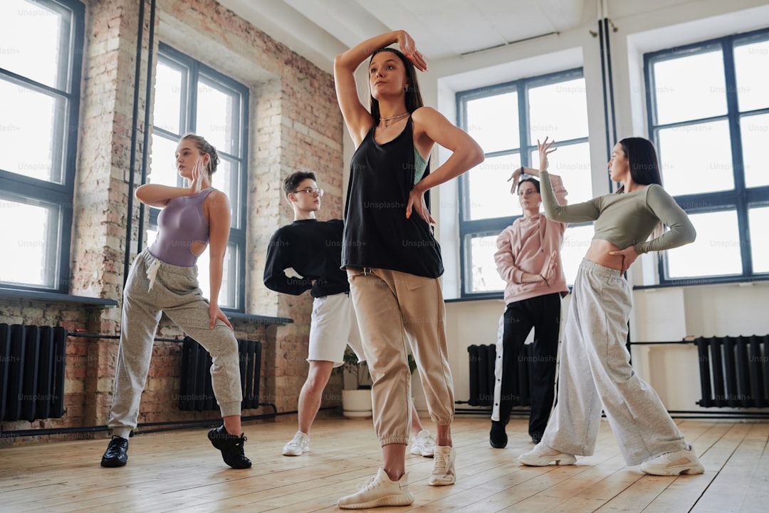 Youthful female performer with arm raised over head standing in front of dance group learning new movements of vogue dancing